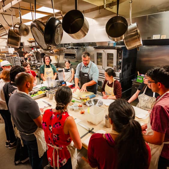 Cooking class participants gathered around a table in a commercial kitchen