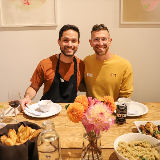 Two diners smiling behind a community table and food spread