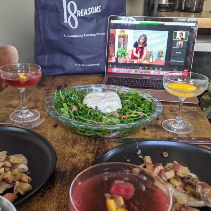 An open laptop showing a livestream of an 18 Reasons cooking class, with food preparation in the foreground
